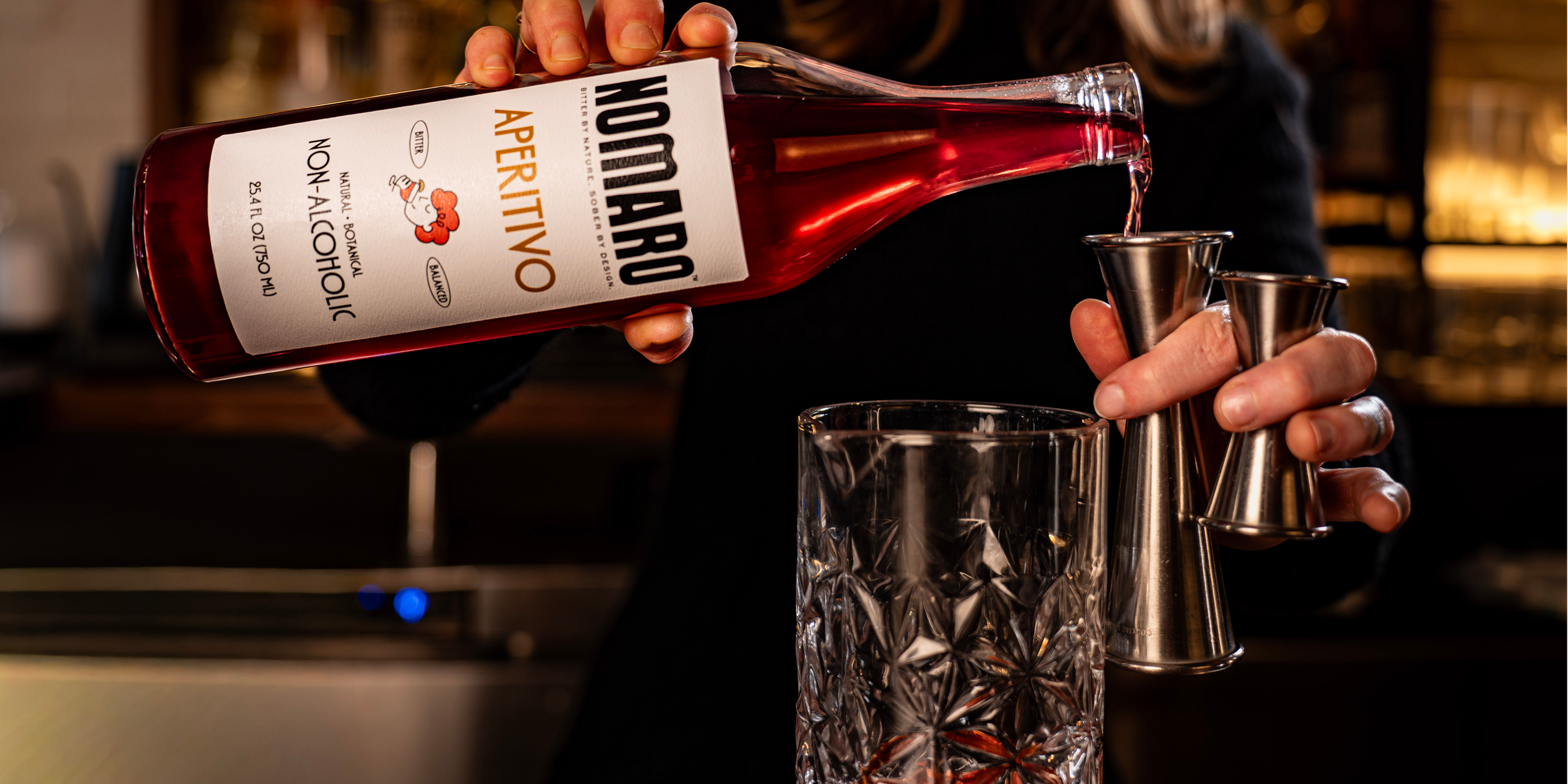Person pouring a bottle of Nomaro Aperitivo into a glass with a blurred background.