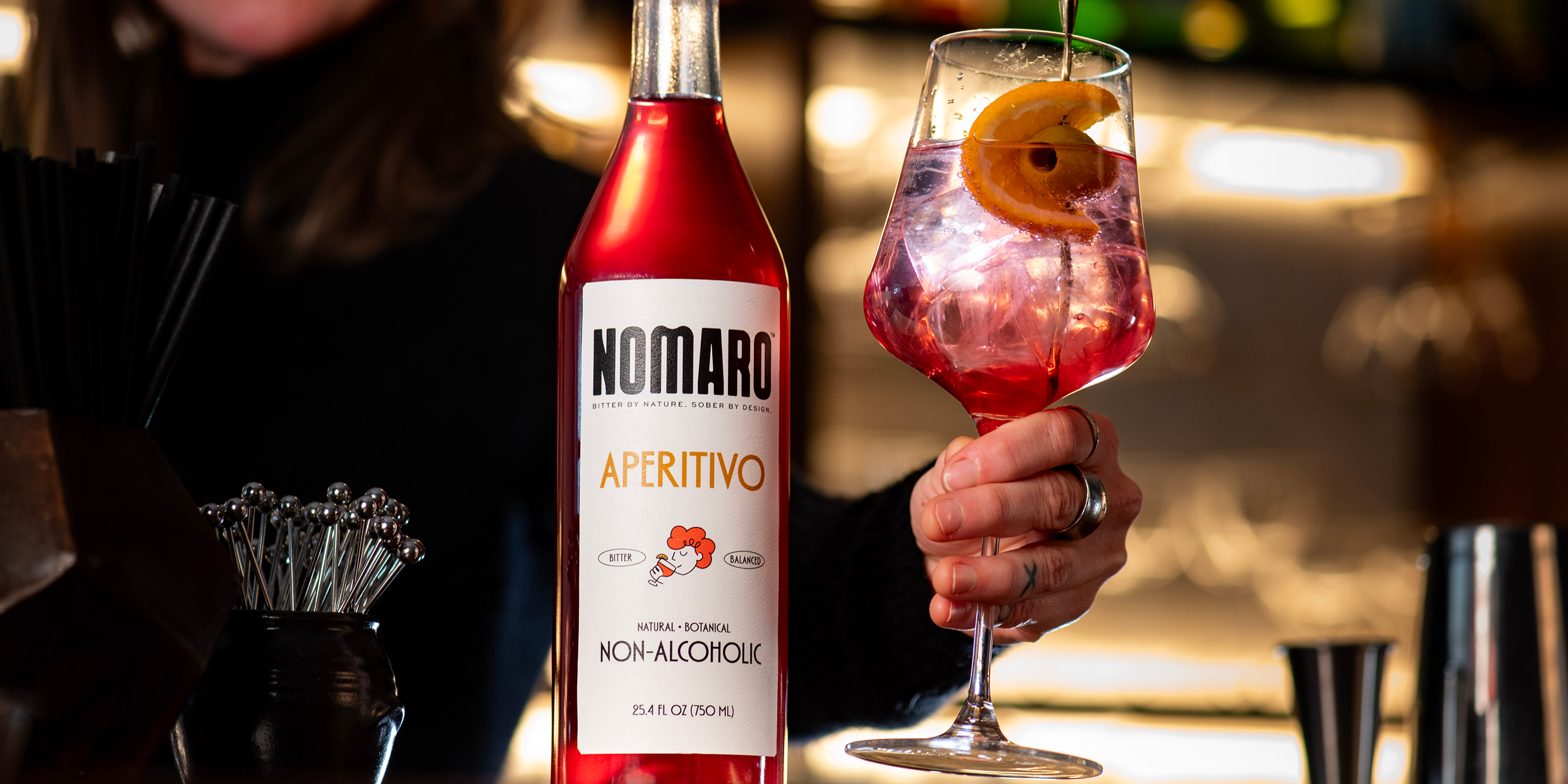 Nomaro aperitivo bottle with a glass of a pink cocktail on a blurred bar background